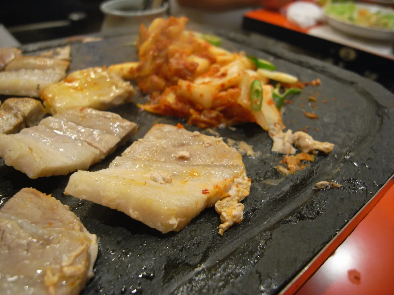 A Korean BBQ table with grilling pork belly and a spread of banchan side dishes
