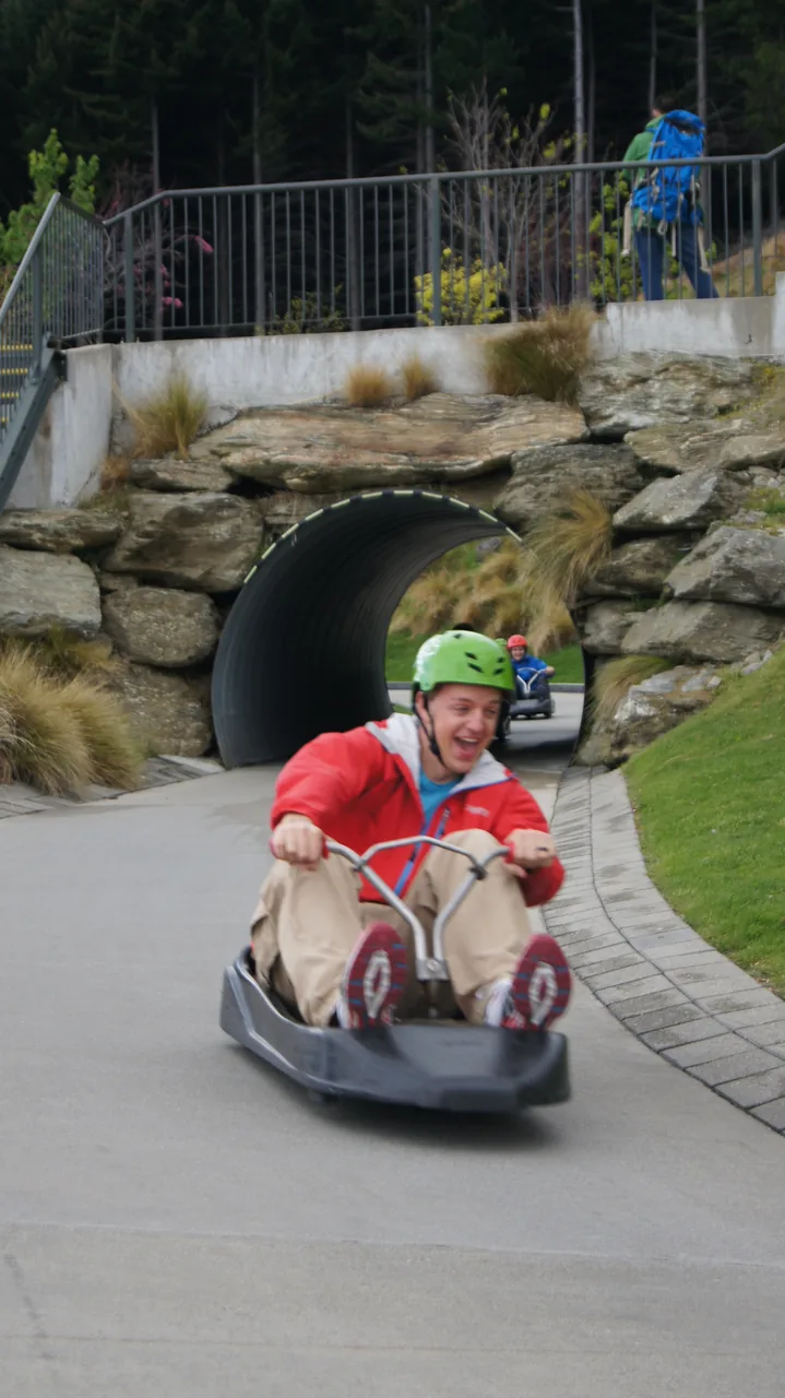 Smiling rider in a helmet steering a Skyline Luge cart out of a tunnel