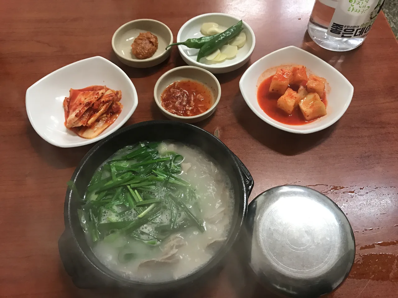 A bowl of dwaeji-gukbap with chives, rice and banchan side dishes