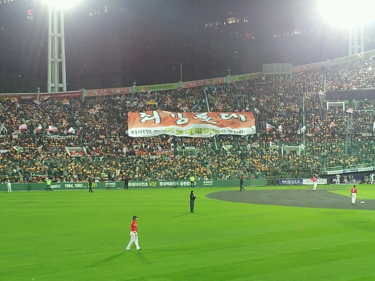 Packed night baseball game at Sajik Stadium in Busan with a huge supporters' banner and floodlights