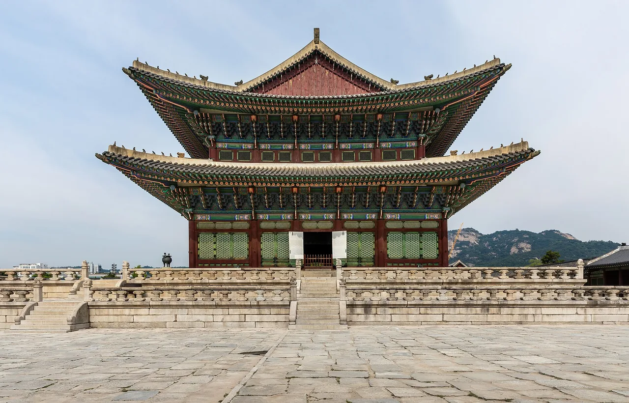 The throne hall Geunjeongjeon at Gyeongbokgung Palace under a blue sky with guards in traditional dress