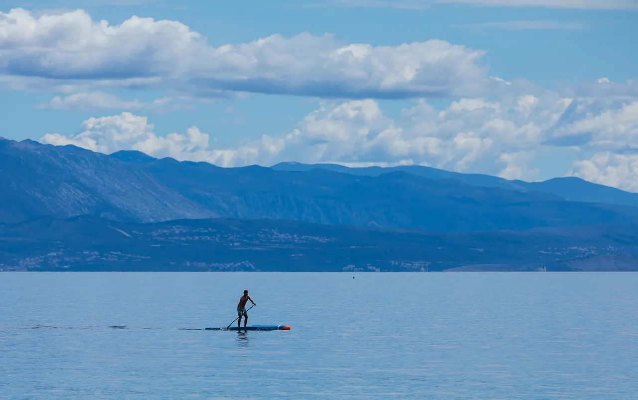 Una persona haciendo paddle surf sobre agua tranquila del mar