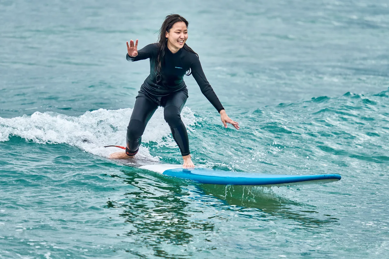 A beginner surfer riding a small whitewater wave on a soft board at a Korean surf beach