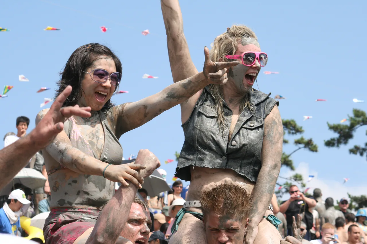 Two friends covered in mud, laughing and celebrating at the Boryeong Mud Festival