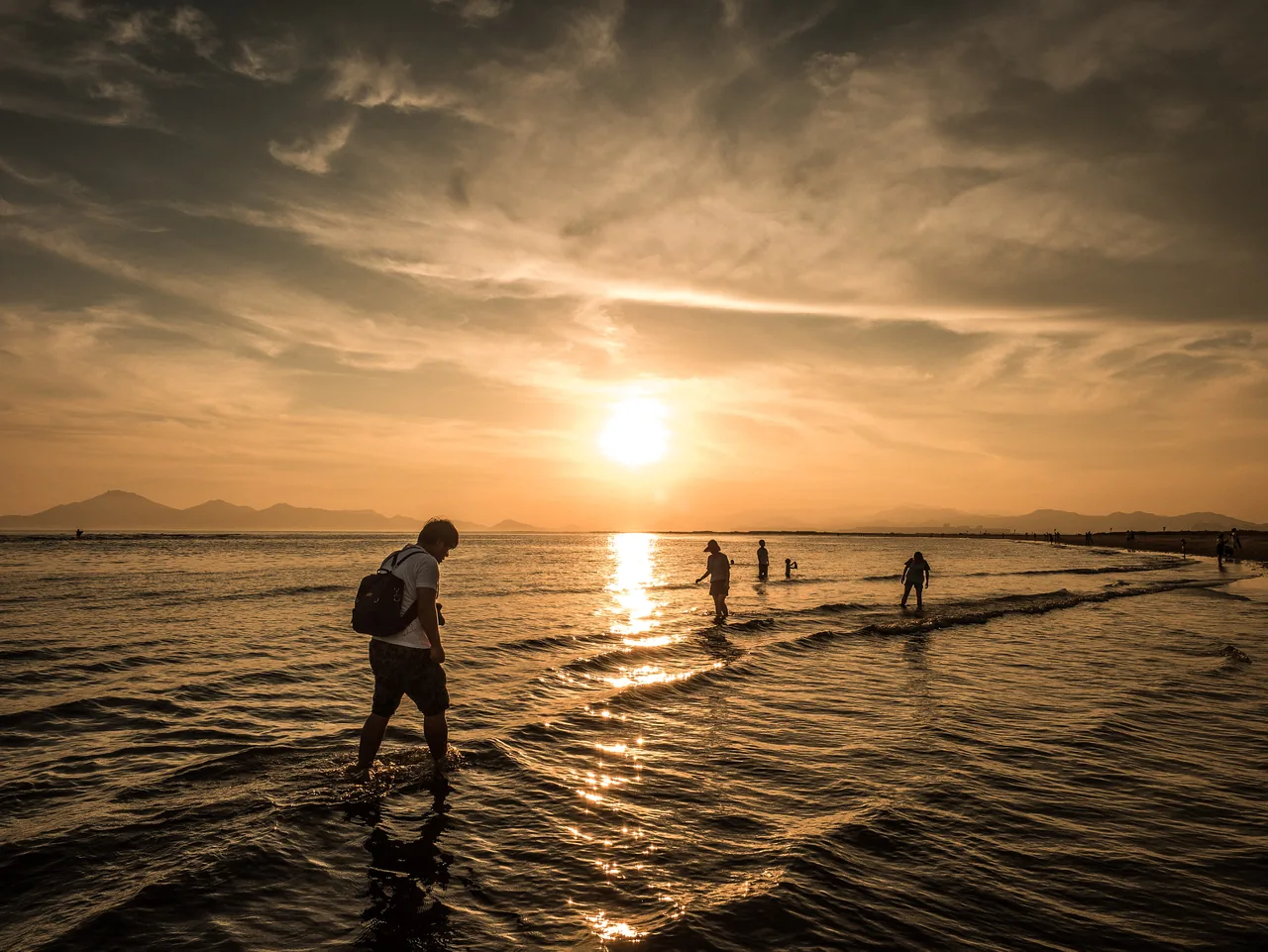 Visitors standing ankle-deep in the shallow water at Dadaepo Beach in Busan as the sun drops, low gold light across the wet sand Visitors standing ankle-deep in the shallow water at Dadaepo Beach in Busan as the sun drops, low gold light across the wet sand