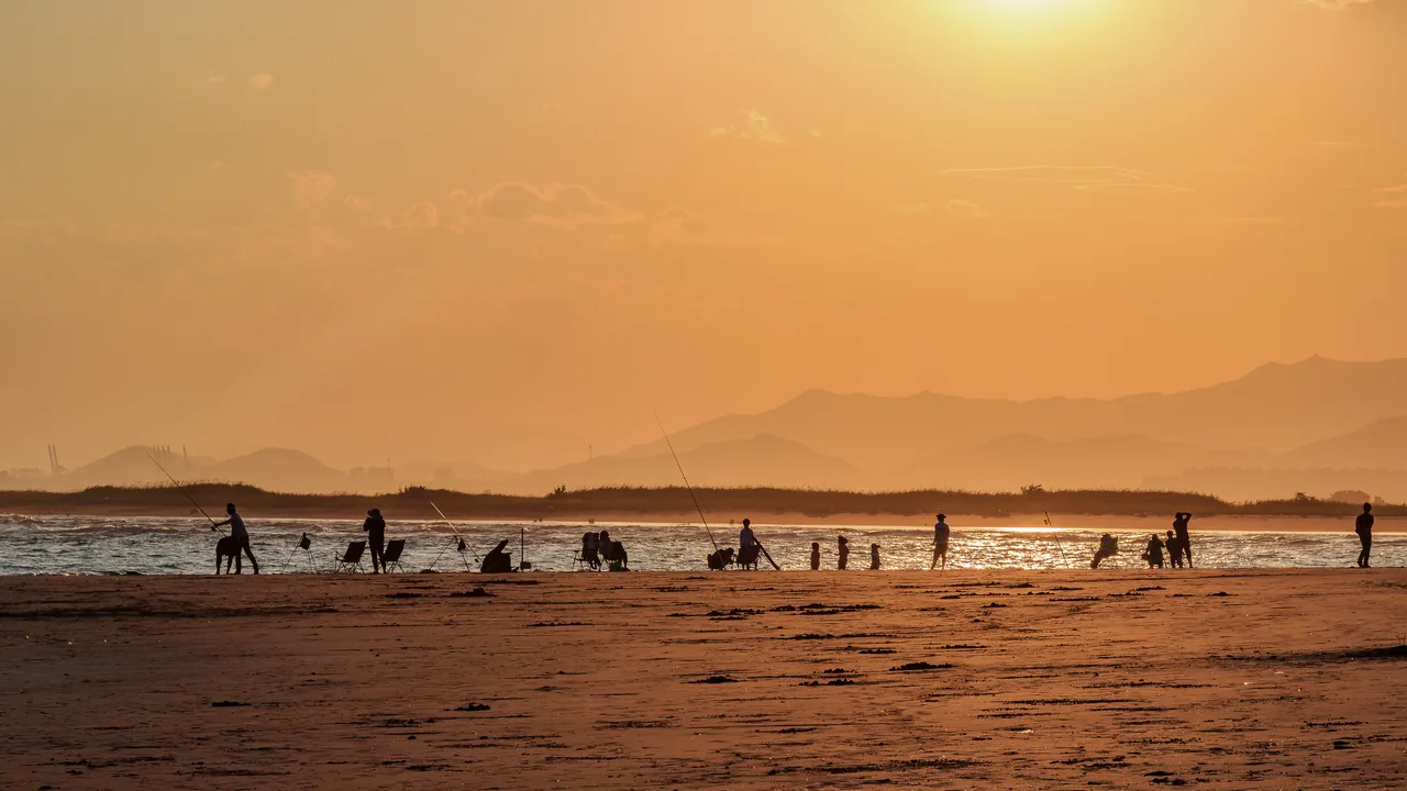 Low tide at Dadaepo, a wide expanse of exposed flats with small figures walking across it under strong golden backlight Low tide at Dadaepo, a wide expanse of exposed flats with small figures walking across it under strong golden backlight