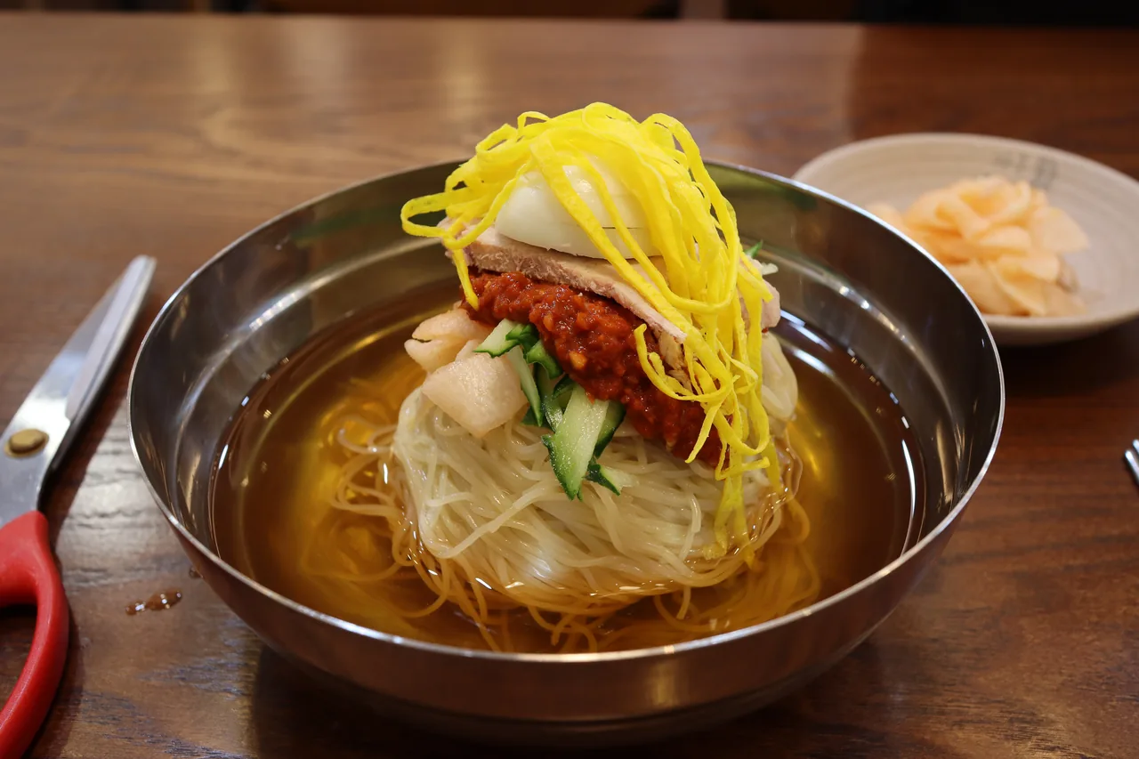A bowl of milmyeon on the table next to a pair of scissors for cutting the noodles A bowl of milmyeon on the table next to a pair of scissors for cutting the noodles