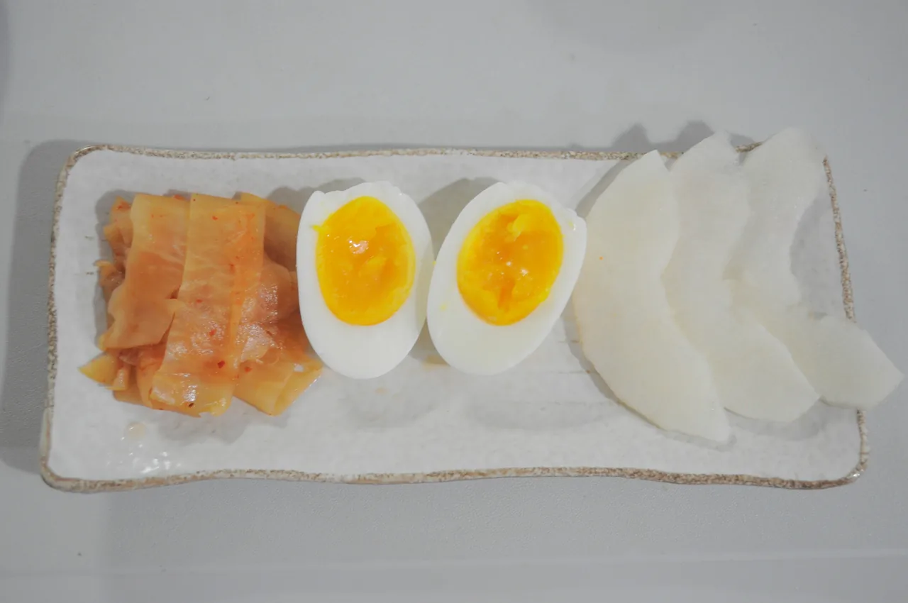 Toppings for cold noodles including pickled radish, kimchi, a boiled egg, and radish slices Toppings for cold noodles including pickled radish, kimchi, a boiled egg, and radish slices