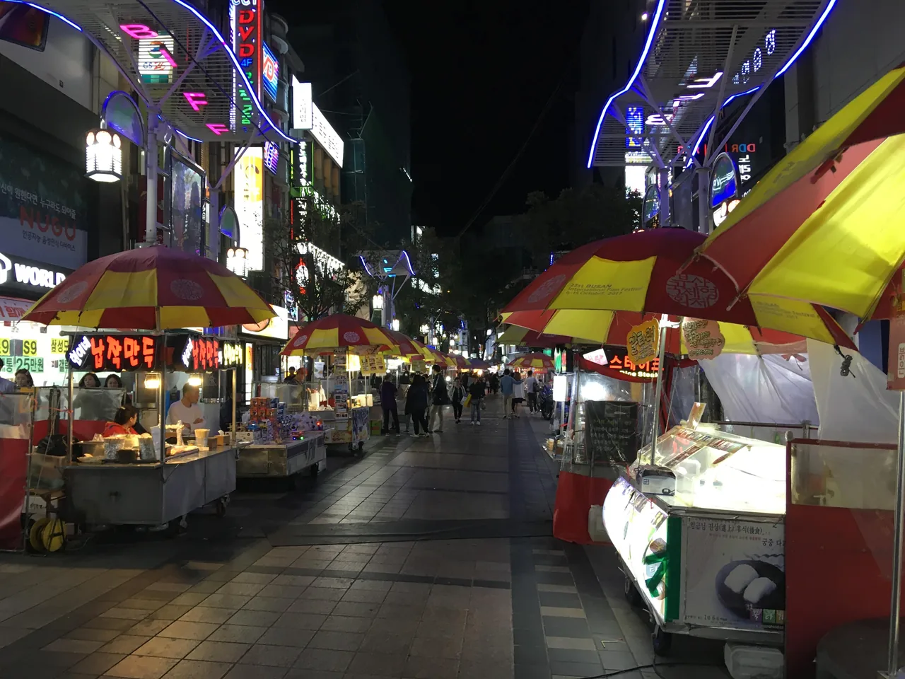 BIFF Square in Nampo-dong at night, rows of red and yellow street food stalls under a blue neon arch