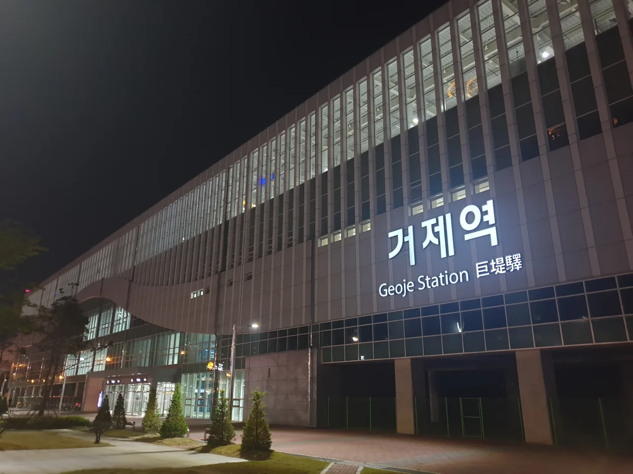 Geoje Station exterior at night, illuminated station sign above a glass facade with nobody outside