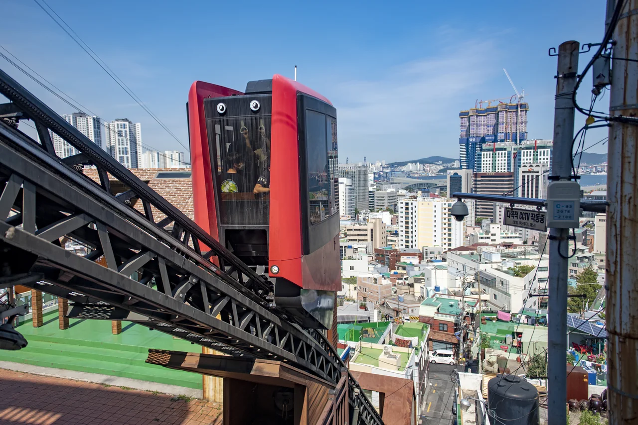 Red monorail cabin standing on a steel track above the hillside neighbourhood with North Port behind