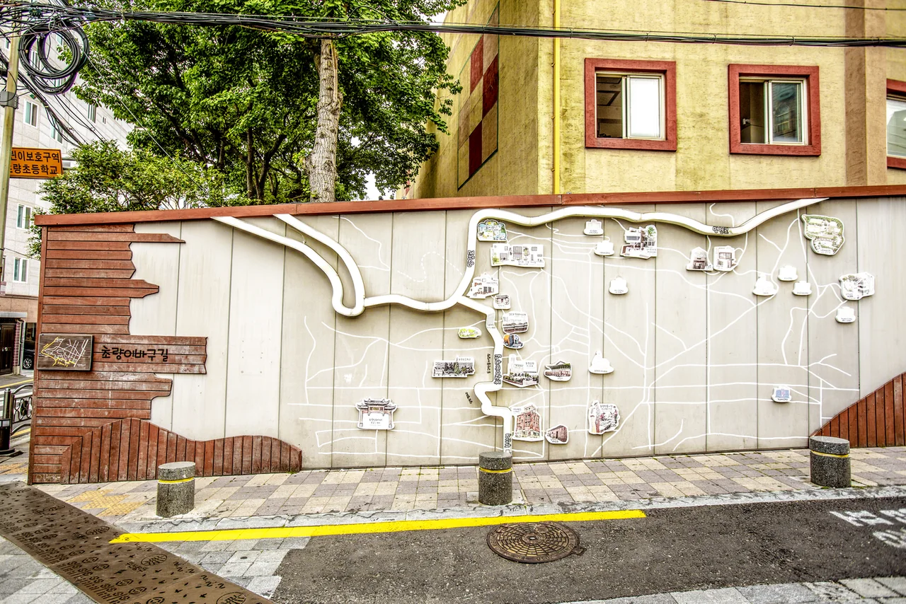 Wooden Choryang Ibagu-gil sign next to a white wall with a relief map of the neighbourhood