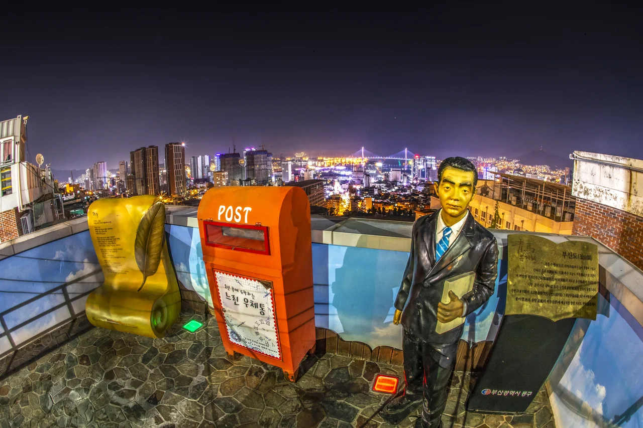 Yu Chi-hwan's red postbox lit at night with the Busan Harbour Bridge glowing behind it