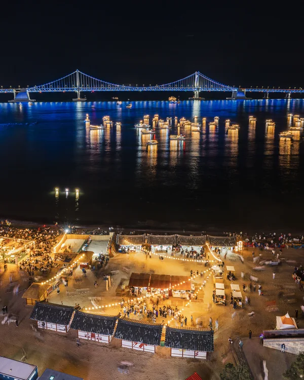 Puestos iluminados y gente en la playa de Gwangalli durante una noche de evento