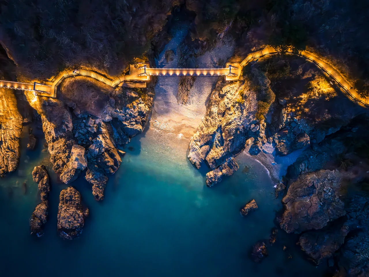 Overhead drone view of the illuminated Igidae suspension bridge above turquoise water