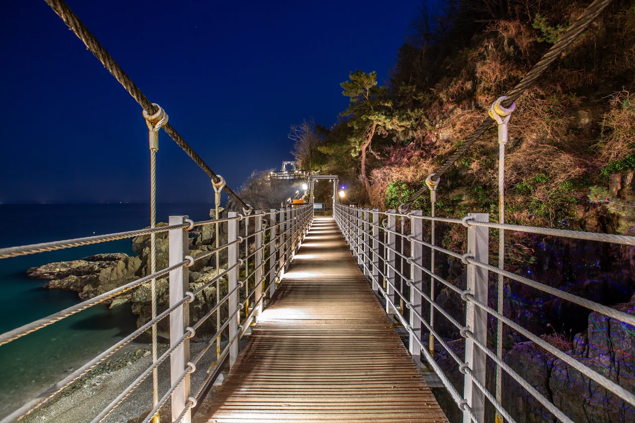 The lit Igidae suspension bridge at night seen from the deck looking forward