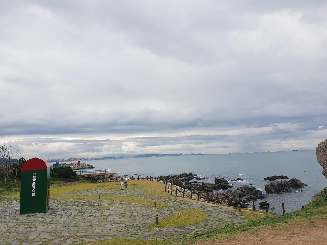 The lawn at Ganjeolgot with the oversized green postbox and the coastal path