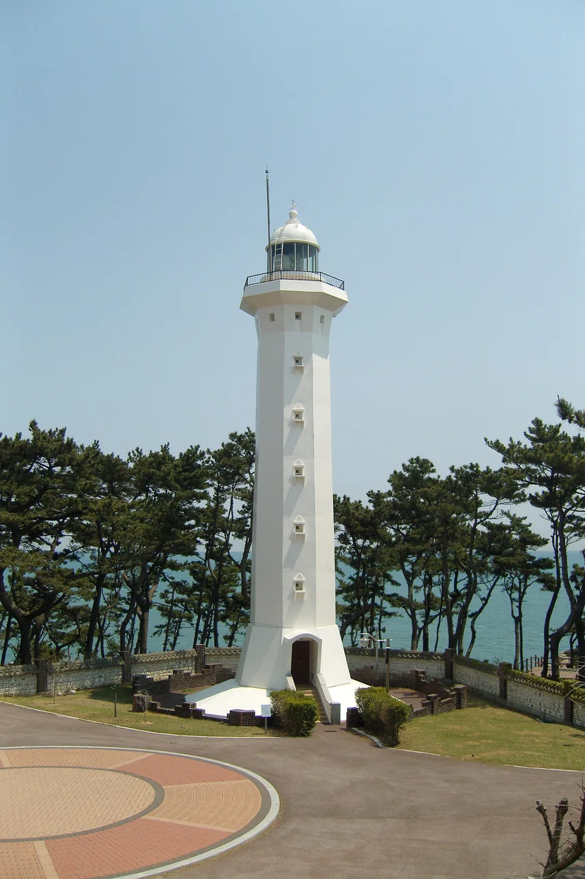 The white working tower of Ulgi lighthouse surrounded by pine trees
