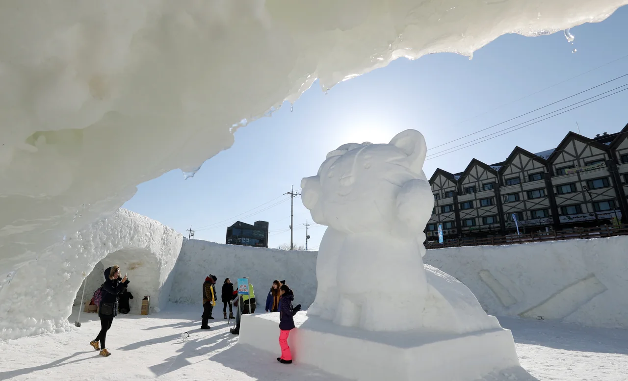 Gran escultura de nieve con forma de oso y una cueva de hielo con visitantes bajo un cielo azul