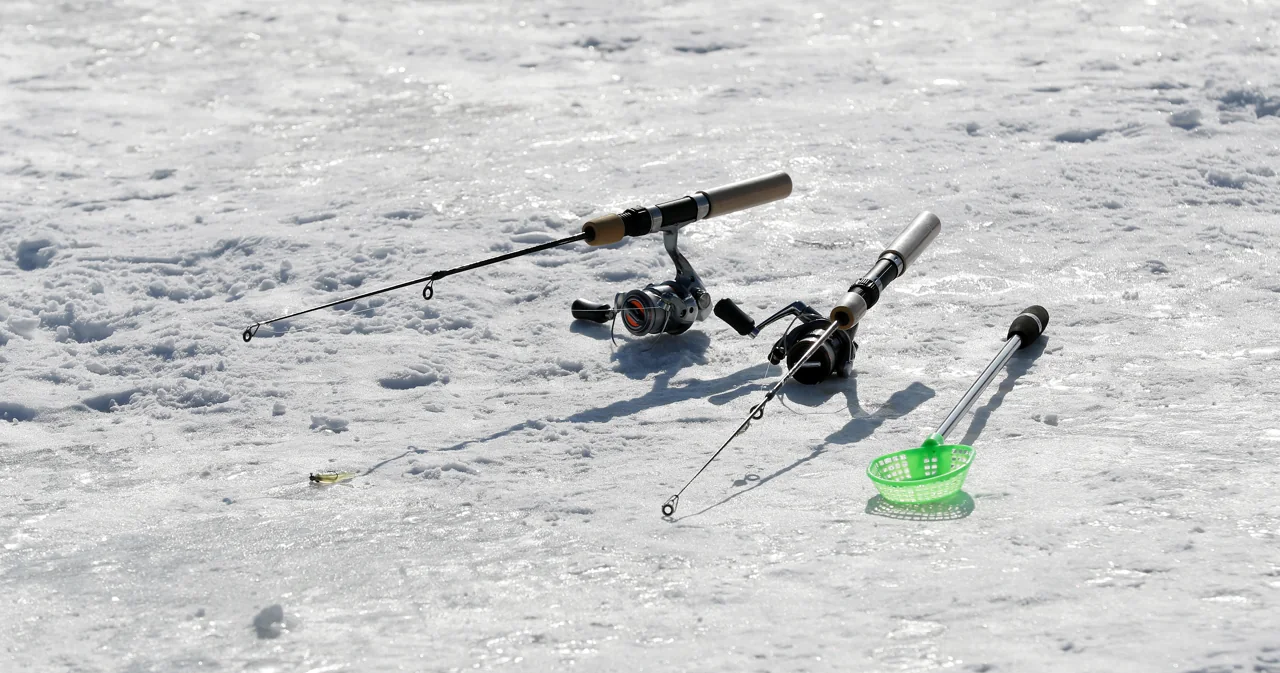 Dos cañas cortas de pesca en hielo y un salabre verde apoyados sobre el hielo, sin personas
