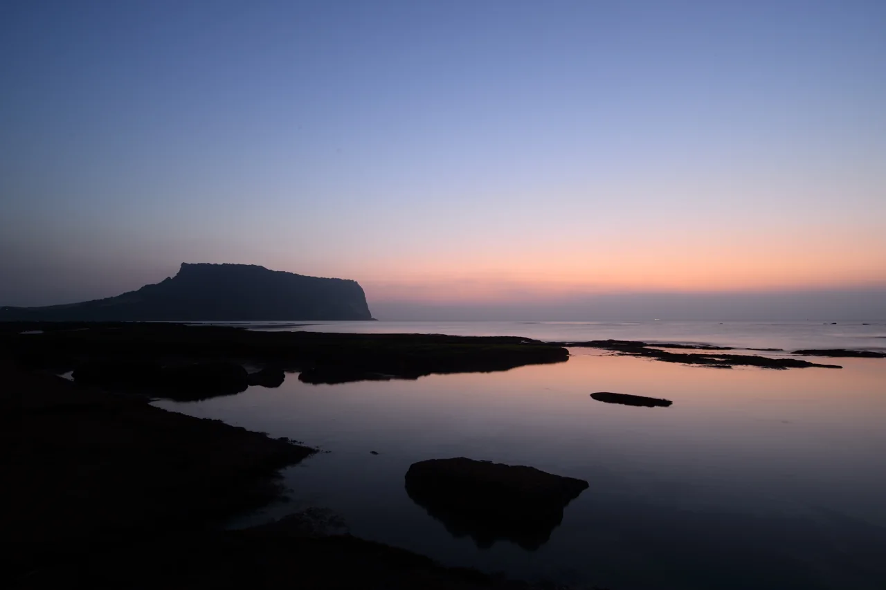 Silueta del pico Seongsan Ilchulbong bajo un cielo anaranjado antes del amanecer, con el mar en calma