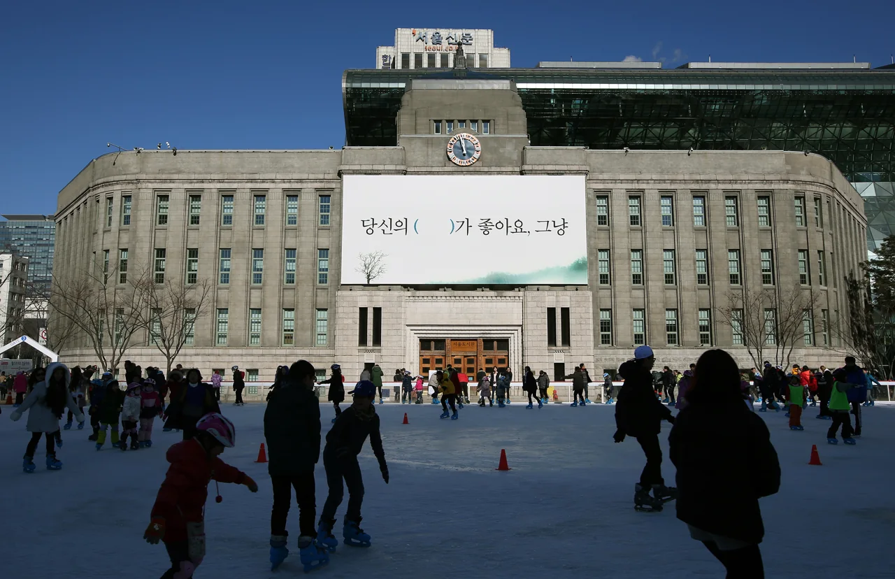 Personas patinando en la pista de hielo de la plaza de Seúl, con el antiguo edificio del Ayuntamiento, hoy Biblioteca de Seúl, al fondo