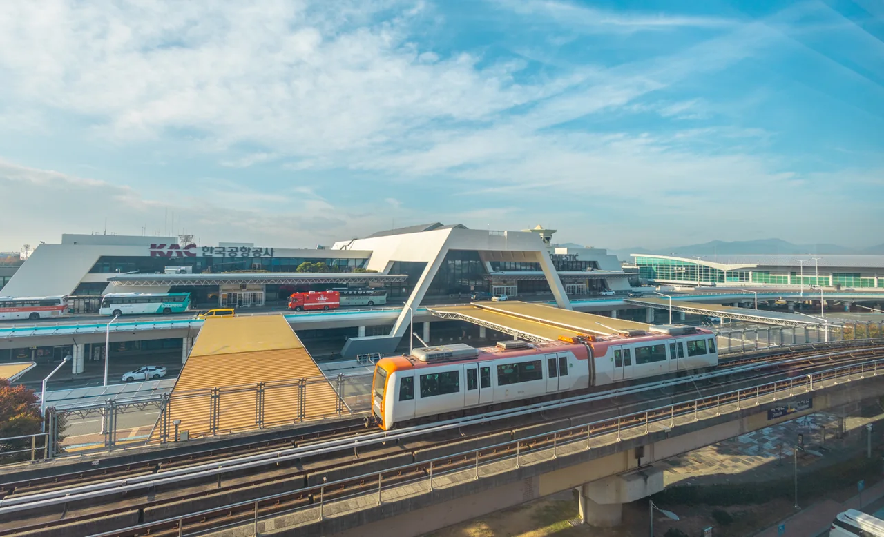 The Gimhae Domestic Terminal with a Busan-Gimhae Light Rail train running on the elevated track in front of it under a clear sky The Gimhae Domestic Terminal with a Busan-Gimhae Light Rail train running on the elevated track in front of it under a clear sky