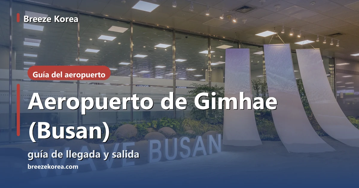Letras iluminadas WAVE BUSAN sobre un jardín interior de arena con piedras redondas y hierba, tres esculturas blancas en forma de tela con degradado azul claro y una pared de cristal con franjas translúcidas al fondo