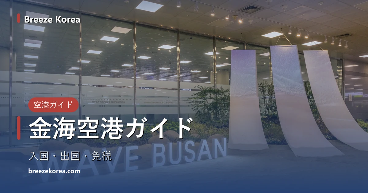 砂を敷いた屋内の庭に光る「WAVE BUSAN」の文字、後ろに水色のグラデーションが入った白い布のような造形が3枚、丸い石と草、その奥に半透明の帯が入ったガラスの壁