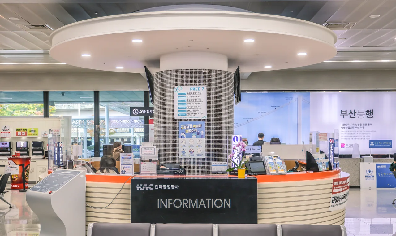 A round information desk with Korea Airports Corporation signage and staff, with a banner hanging behind it A round information desk with Korea Airports Corporation signage and staff, with a banner hanging behind it