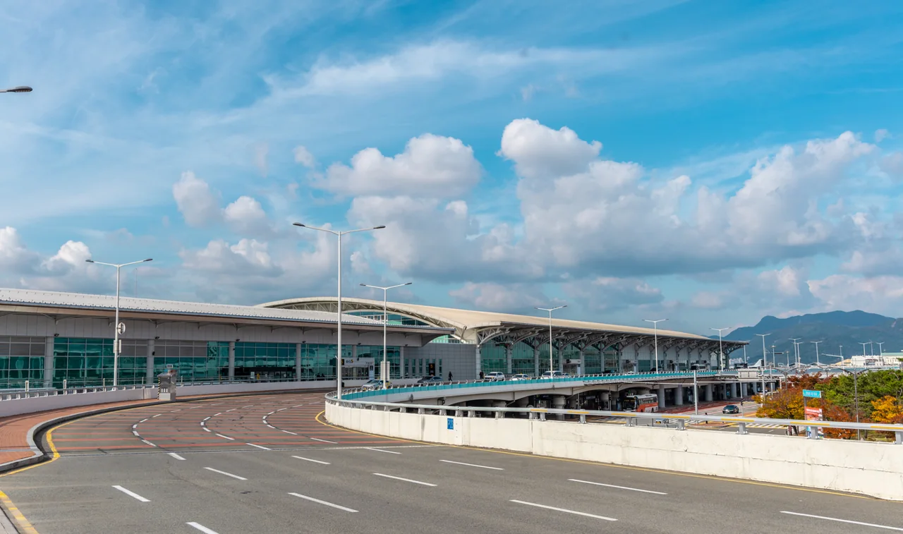 Elevated approach road in front of the long curved roof of the Gimhae International Terminal under a blue sky Elevated approach road in front of the long curved roof of the Gimhae International Terminal under a blue sky