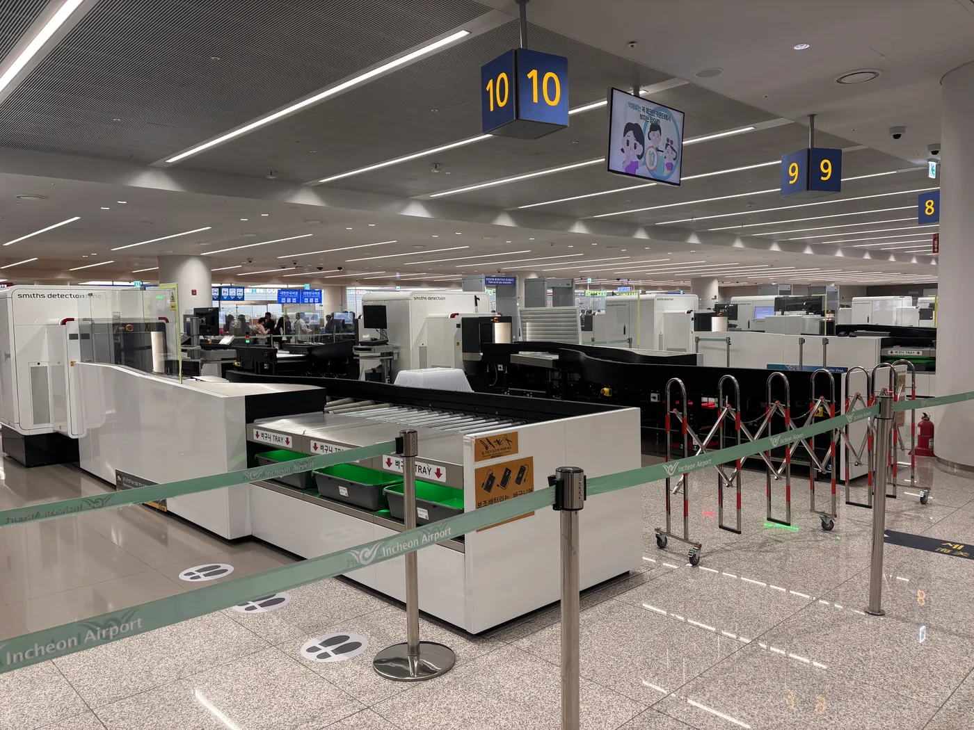 第2旅客ターミナルの保安検査場。天井にレーン番号の「10」「9」「8」、白いCT型の検査機、トレイの返却台、列の仕切り、床の足跡のステッカー