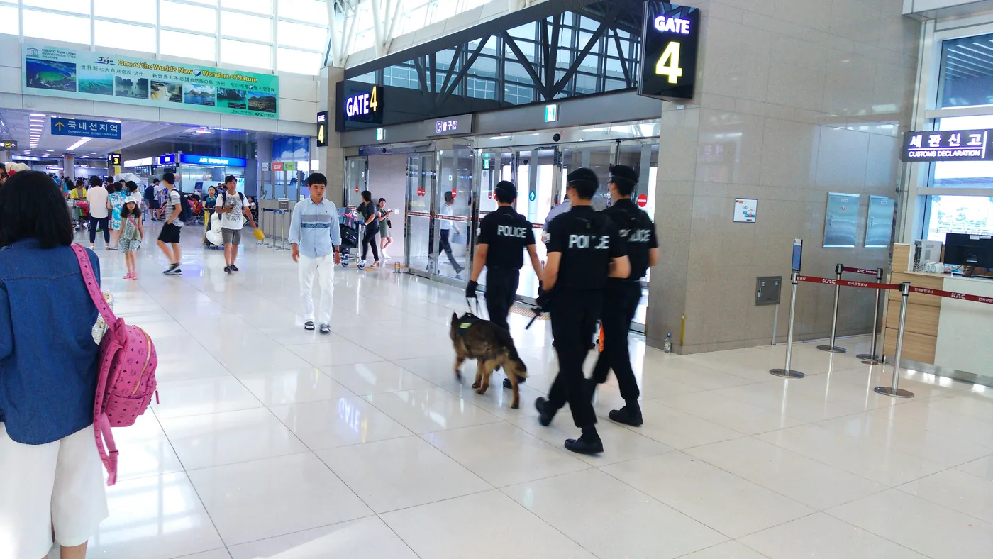 國內線航廈大廳,後方有AIR BUSAN、JEJUair、JINAIR櫃台招牌,柱子上寫著GATE 3,右邊是GATE 4出入口,兩名警察帶著偵測犬走過,旁邊有旅客 國內線航廈大廳,後方有AIR BUSAN、JEJUair、JINAIR櫃台招牌,柱子上寫著GATE 3,右邊是GATE 4出入口,兩名警察帶著偵測犬走過,旁邊有旅客