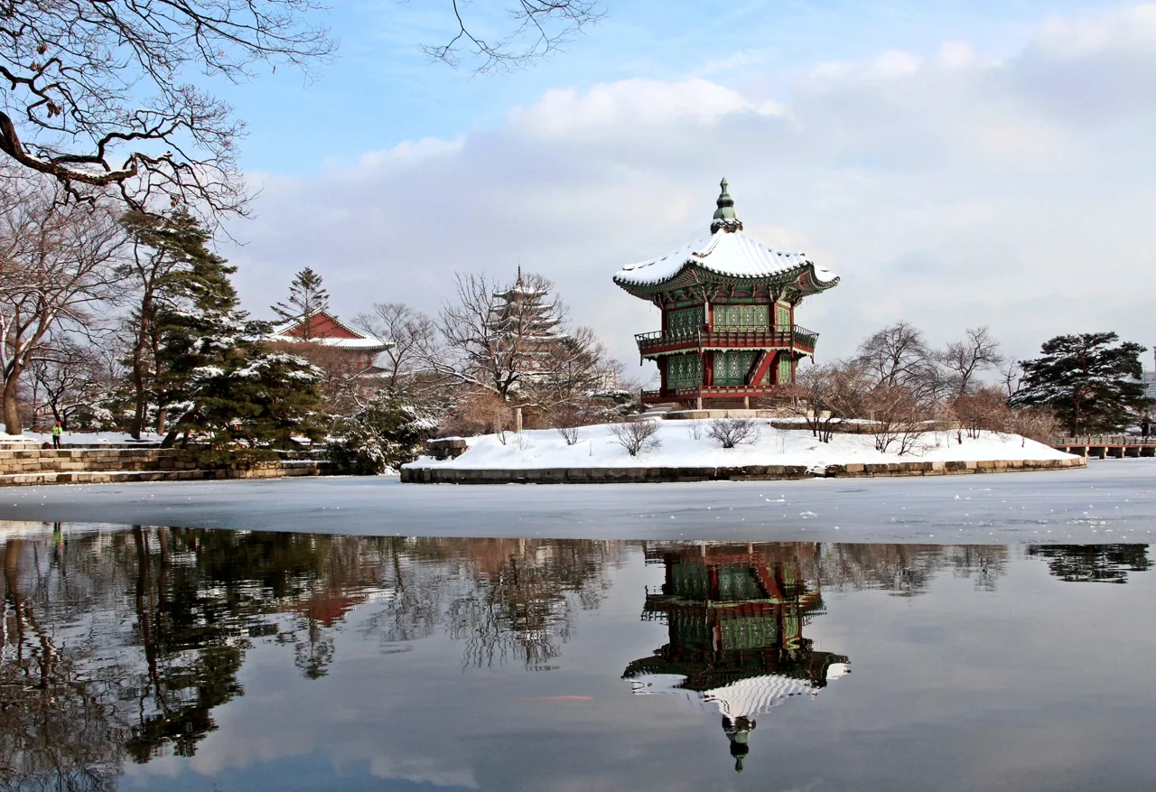 Hyangwonjeong pavilion and its bridge covered in snow, reflected in the pond, with bare winter trees around